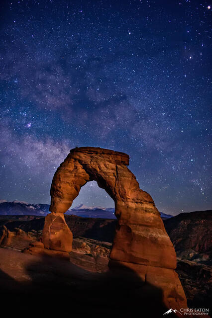 The crescent moon sets in the west at midnight painting Delicate Arch in Arches National Park, the center of our Milky Way Galaxy rises in the southeast .