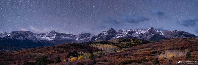 Moonlit mountains below a night sky full of stars.