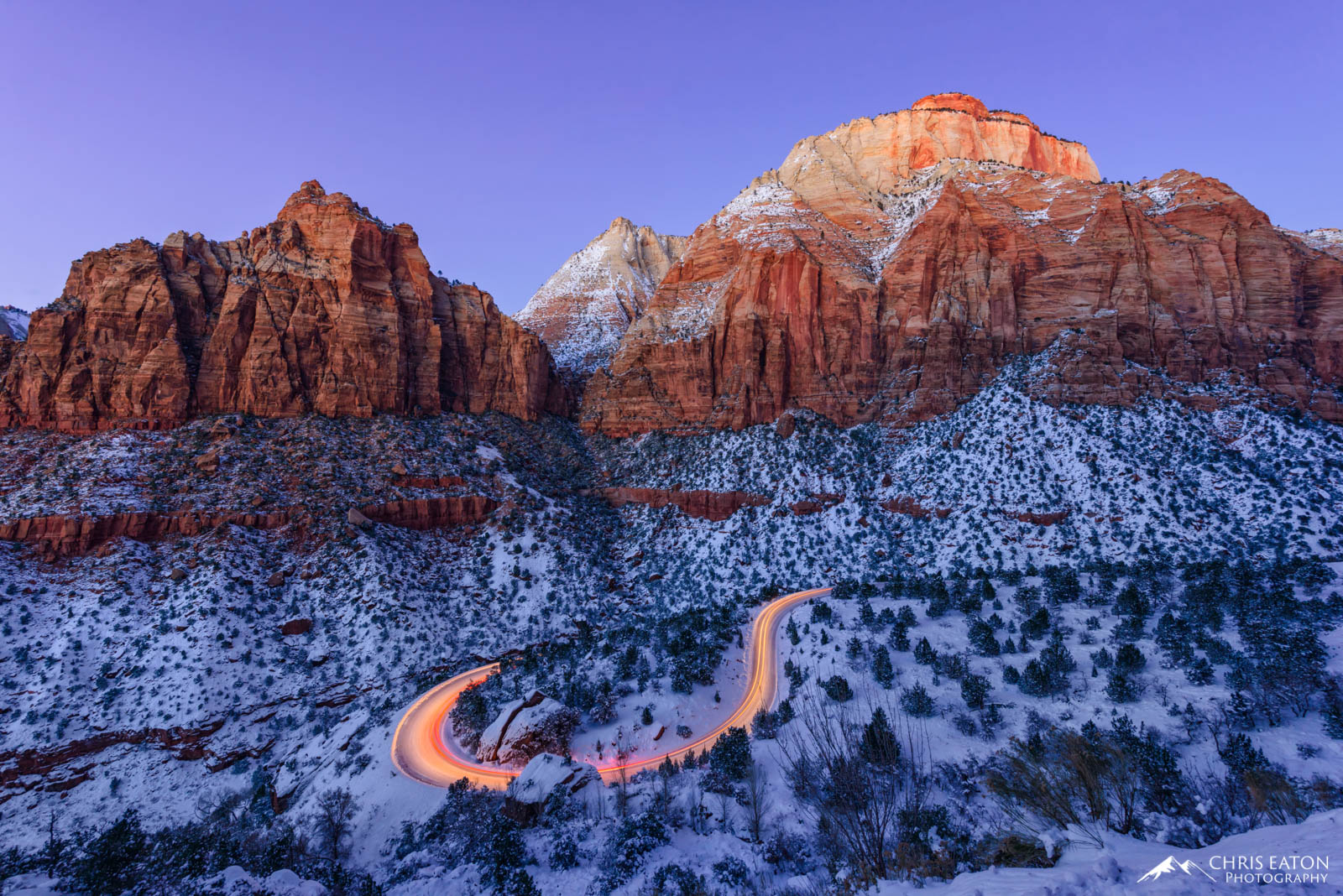 A car's light trail along a winding road in snowy Zion National Park.