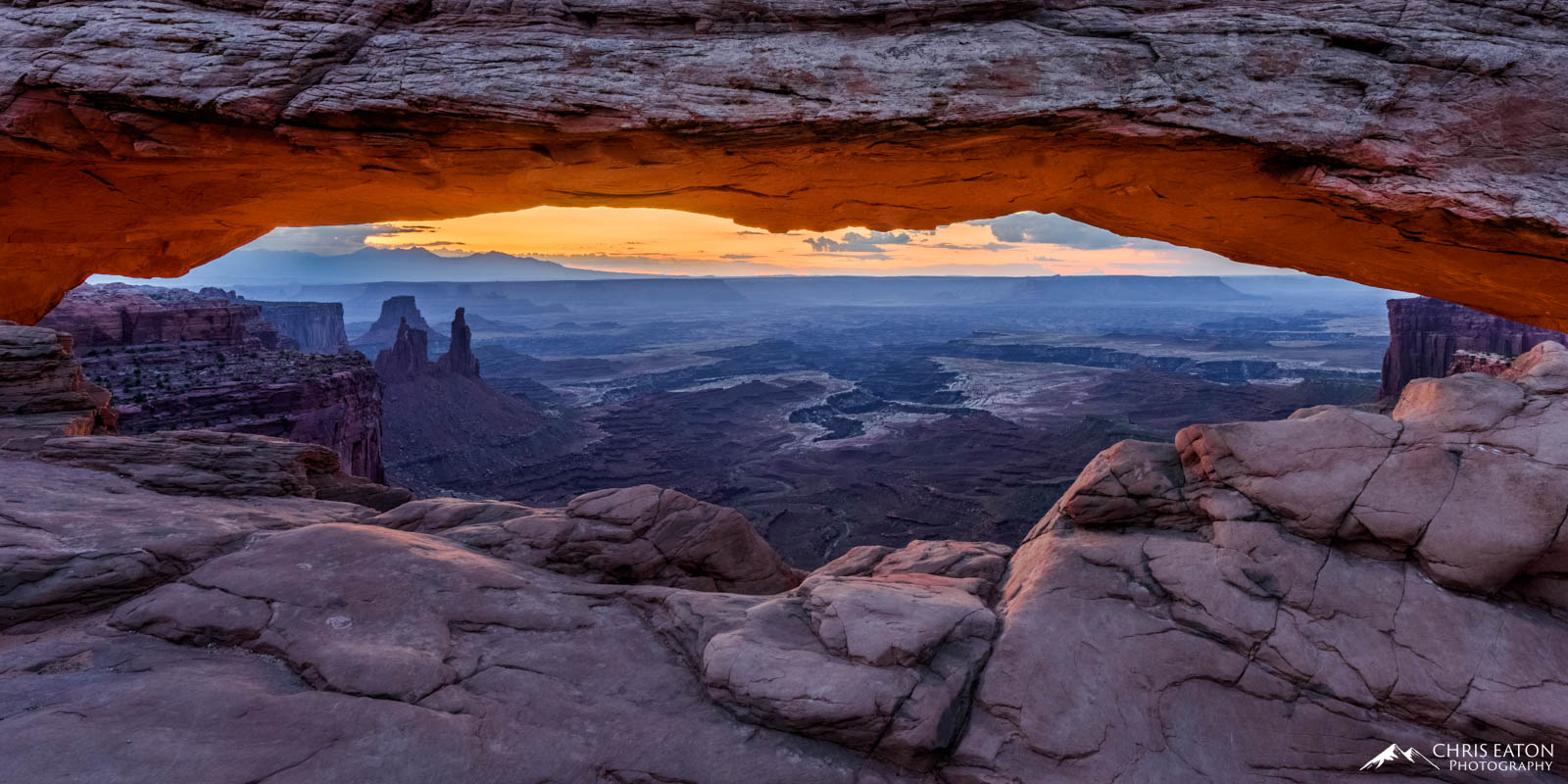 The first orange hues of sunrise light are enough to light up the underside of Mesa Arch in Canyonlands, National Park. Perched...